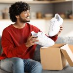 Portrait of happy young indian man unboxing parcel with shoes at home