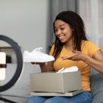 Unboxing video. Black female blogger unpacking parcel with new shoes, recording content for her blog on cellphone